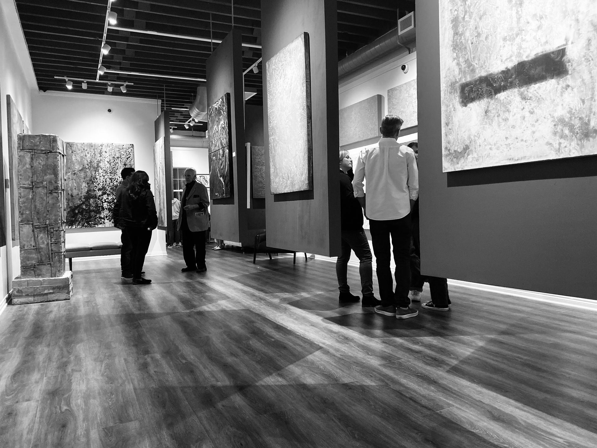 People standing in an art gallery, observing various large paintings displayed on the walls.