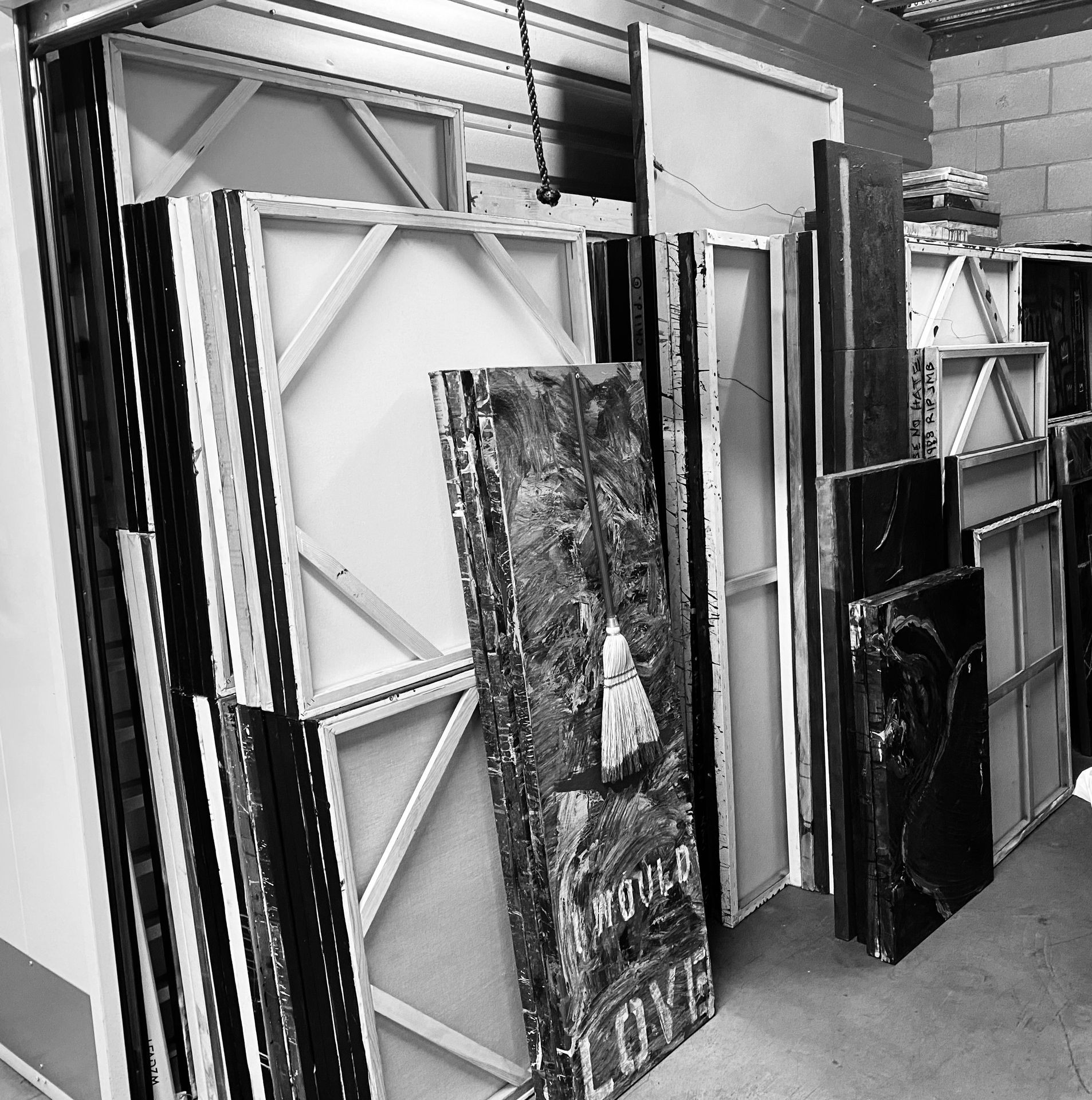 Stack of large blank canvases and painted artworks leaning against a wall in a storage area.